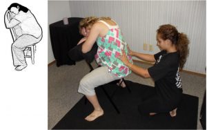 A Madriella student demonstrates how to massage the lower back while their client is sitting backwards in a chair.